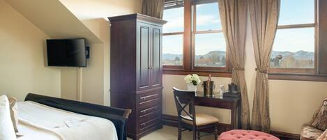 A bedroom with a bed, a desk, a chair, a red ottoman, a wardrobe, and a TV mounted on the wall.