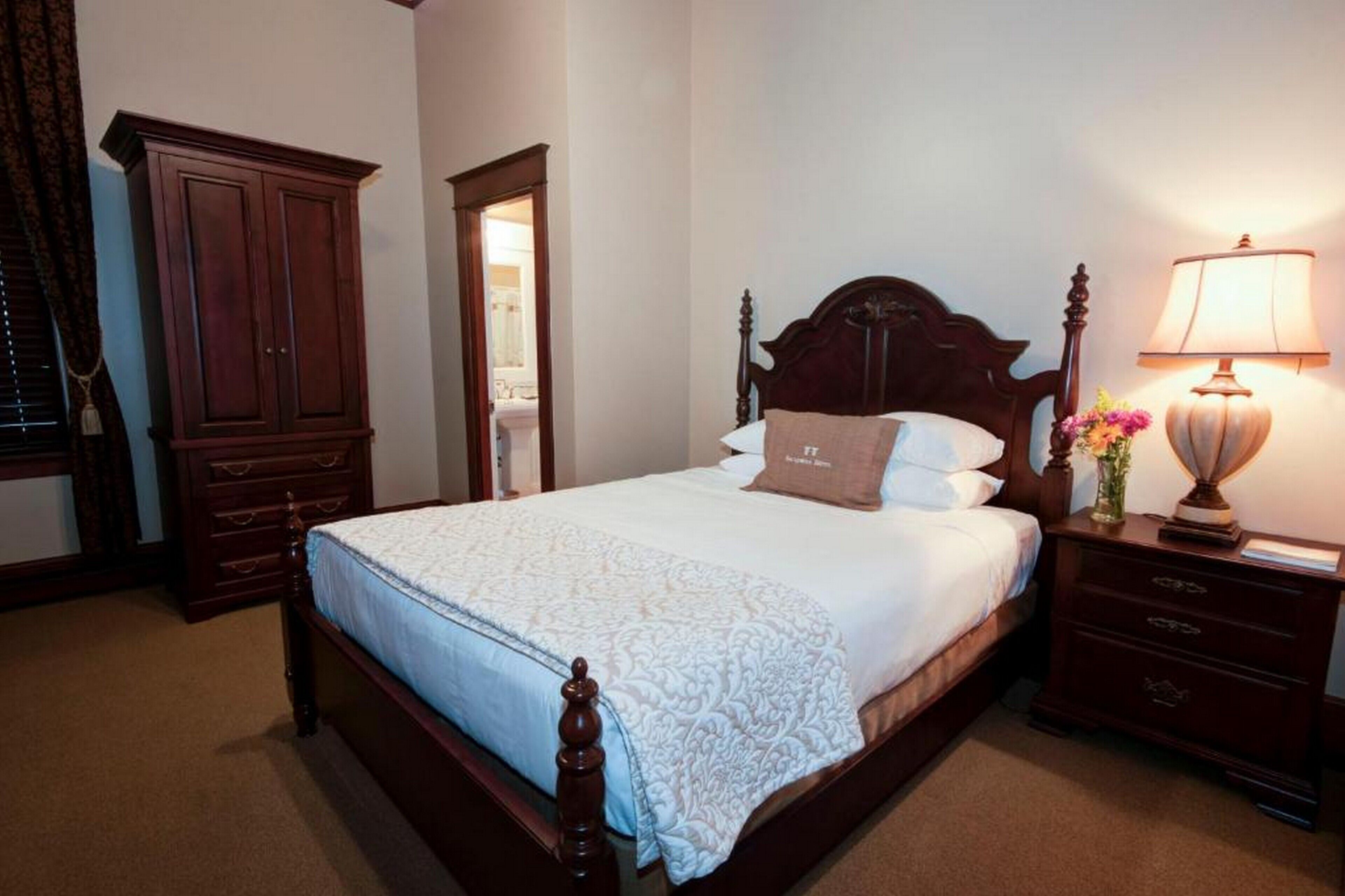 Una cama bien tendida con cabecera de madera, una lámpara de noche y una mesita de noche.