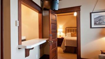 A narrow hallway with a wooden door leading to a bedroom. A small shelf is mounted on the wall, and a framed picture hangs on the adjacent wall.