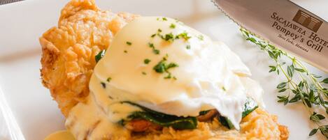 A plate with a fried chicken sandwich, a poached egg, and a side of sauce.