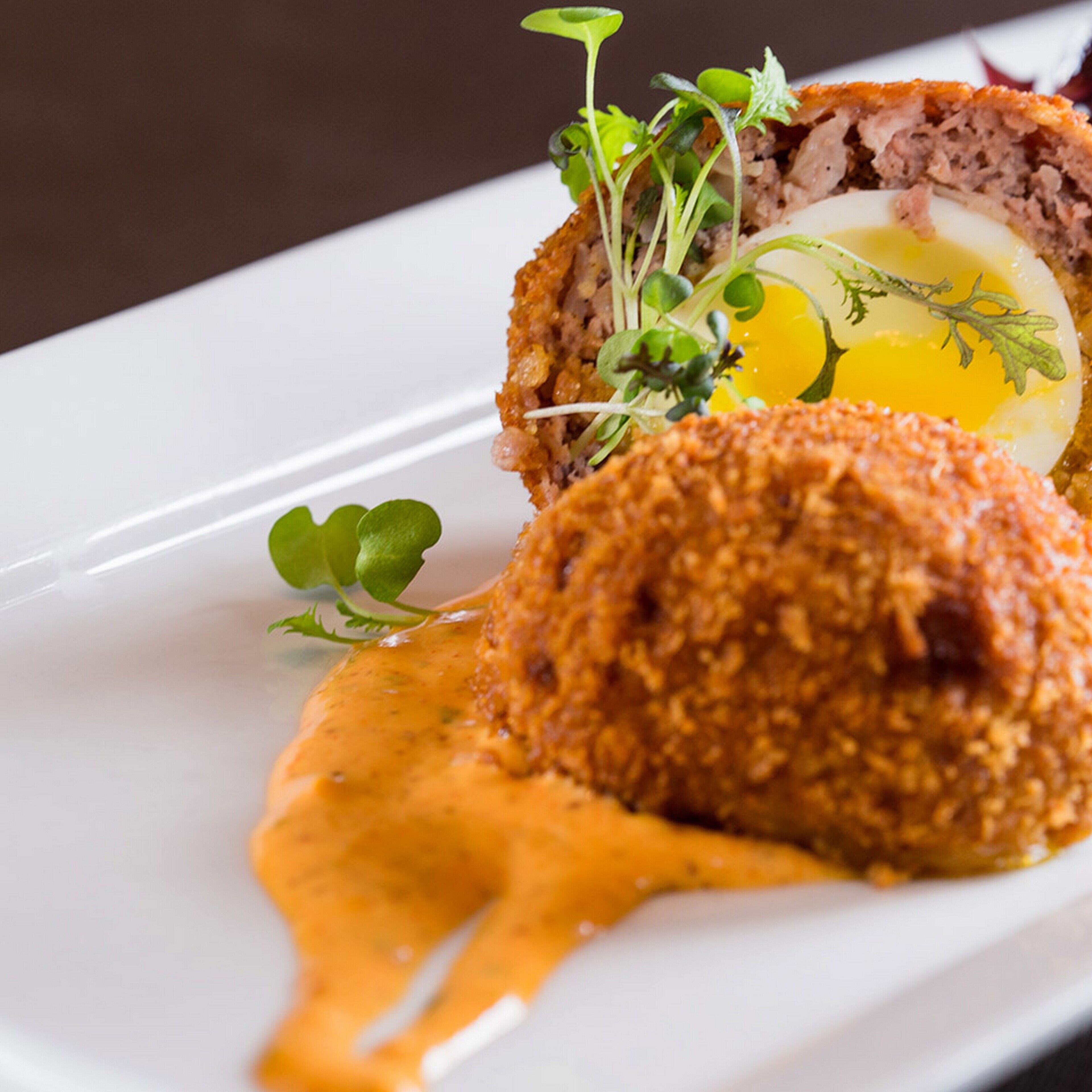 A plated dish with a breaded item, egg, and greens.
