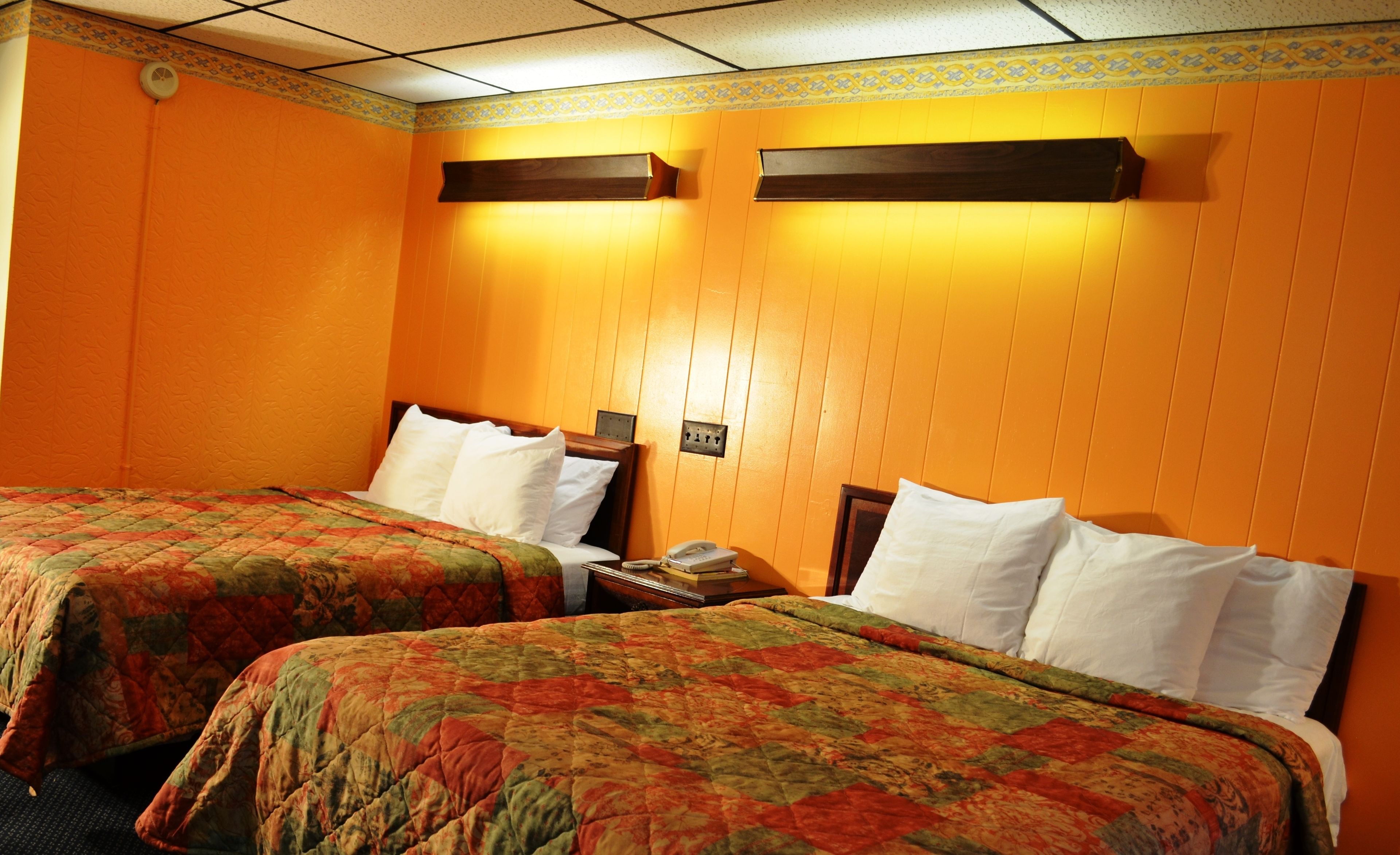 Habitación de hotel con dos camas, cada una con colcha de estampado floral, una mesita de noche con lámpara y un teléfono fijo en la pared.
