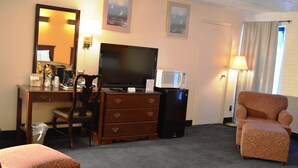 A hotel room with a desk, television, microwave, and a floral armchair. - Economy Inn (Bluefield)
