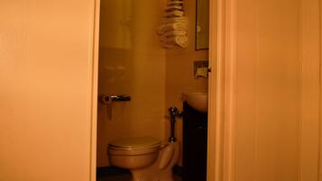 Un bany petit amb vàter, un lavabo i una pila de tovalloles a la paret.