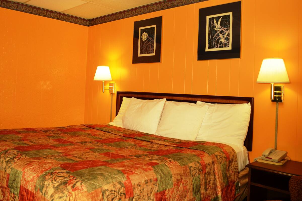 A hotel room with a large bed, two wall-mounted lamps, and two framed pictures on the wall.