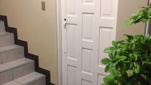 Une porte blanche avec une poignée de porte, un paillasson noir et un escalier avec des marches de couleur beige menant à la porte.