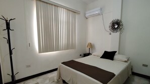 Une chambre à coucher comprenant un lit, une fenêtre avec des stores, un climatiseur, une lampe et un élément décoratif mural.