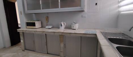 Una cocina con suelo de piedra, microondas, hervidor y lavabo.