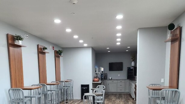 Una habitación amplia con suelo de madera, varias zonas de estar con sillas, una mesa central y una cocina con armarios y televisor.