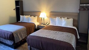 Habitación de hotel con dos camas, una mesita de noche con lámpara, un armario y una lámpara colgante.