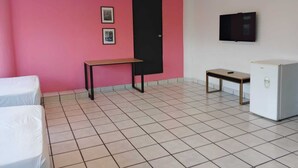 A room with a pink wall, a black door, a TV mounted on the wall, a small table, a refrigerator, and two beds. - Unidades Privadas con AC-TV-WiFi y Estacionamiento en Centro de MTY (Monterrey)