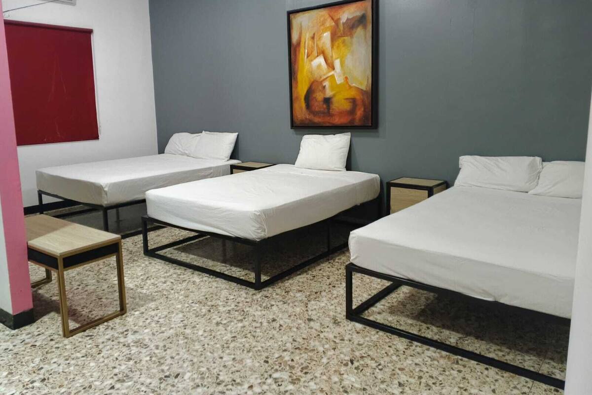 Habitación de hotel con tres camas individuales, una puerta roja, un cuadro en la pared y una mesita pequeña.