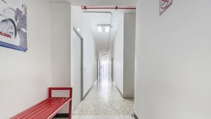 A hallway with a red bench, white walls, and a tiled floor. - Unidades Privadas con AC-TV-WiFi y Estacionamiento en Centro de MTY (Monterrey)