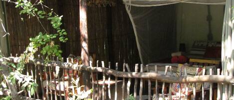 A rustic wooden fence with a woven canopy, a wooden bench, and a small table with books and a red object.