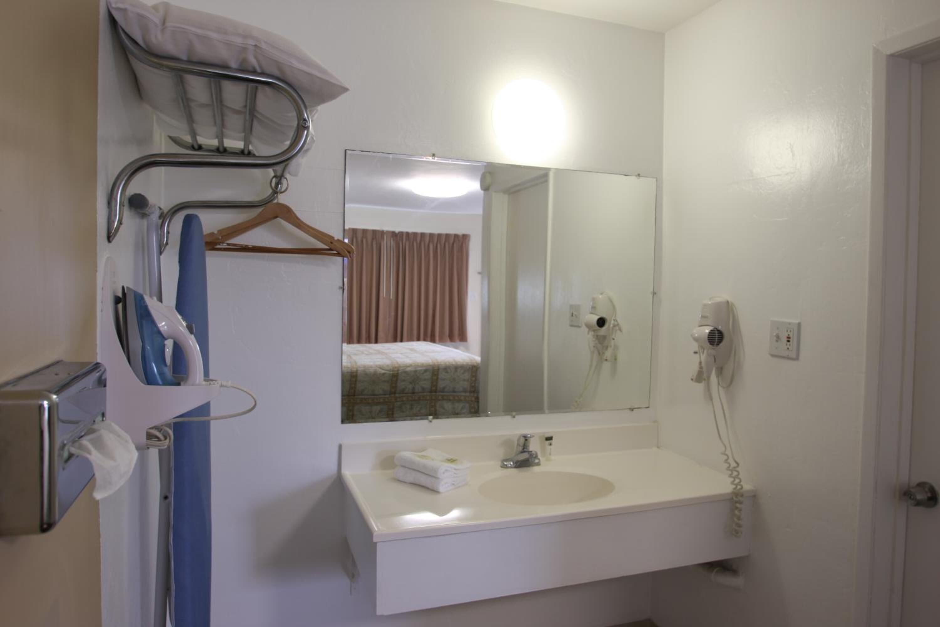 Un baño con lavamanos blanco, espejo, toallero, secador de pelo y ducha.