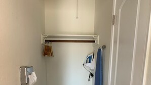 A narrow hallway with a wooden floor, a white door on the right, and a small shelf with a tissue dispenser on the left. - Redwood Inn (Santa Rosa)