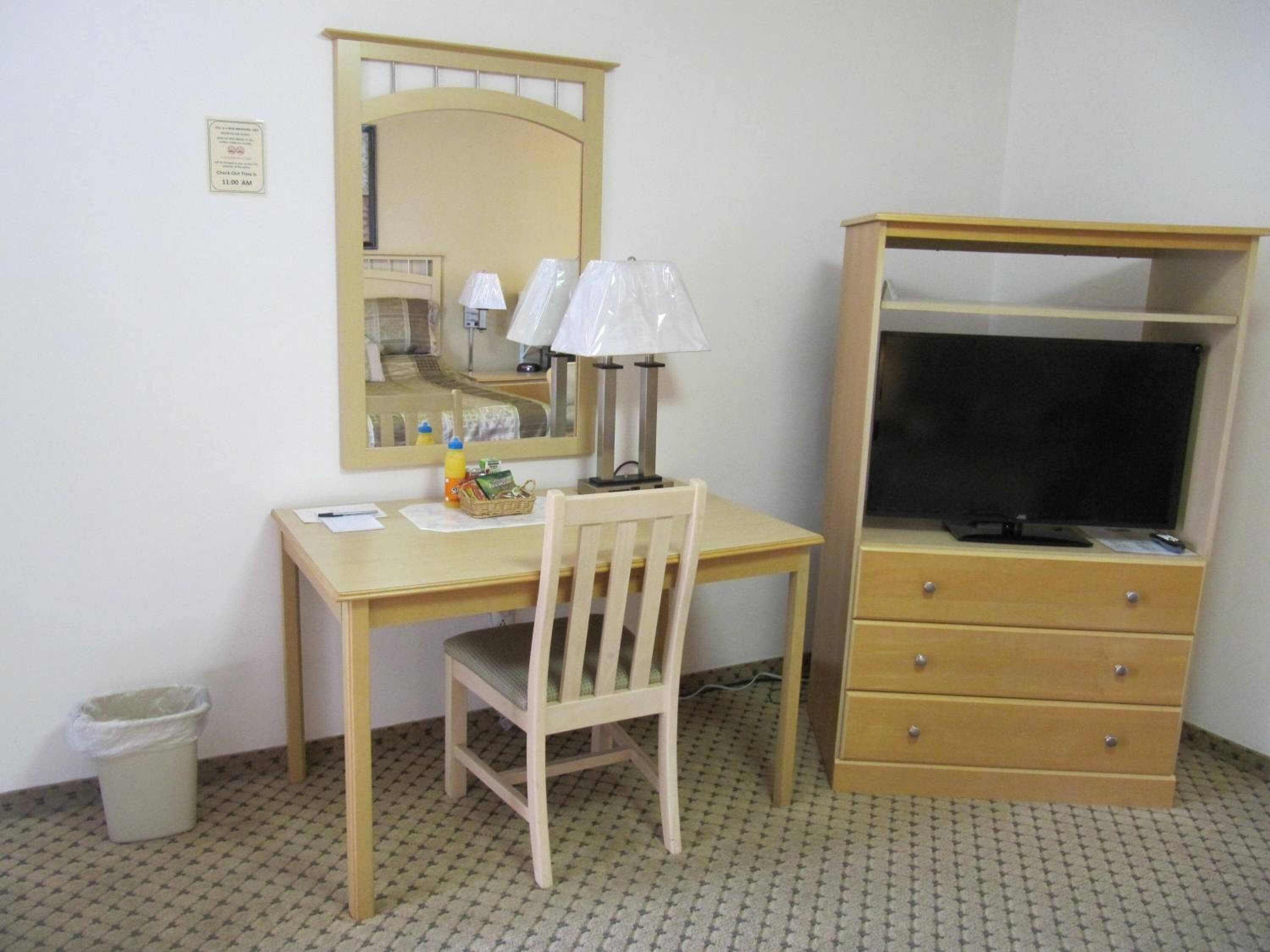 A small, tidy room with a wooden desk, a chair, a mirror, a lamp, a television, and a dresser.