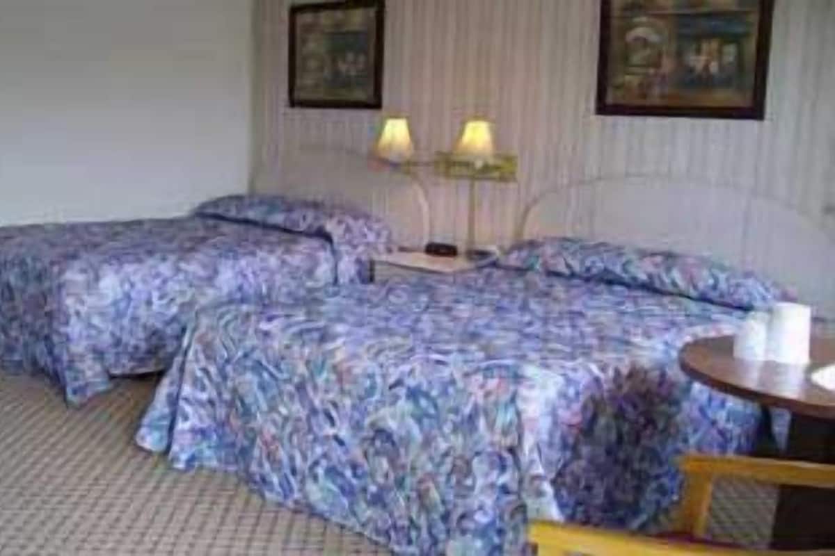 A hotel room with two beds, a small table, and two lamps.