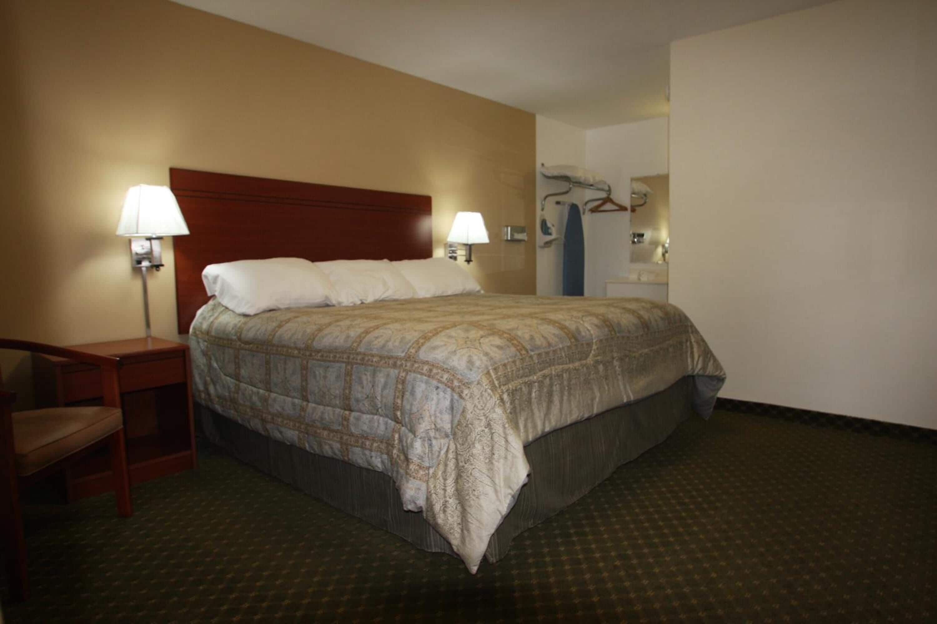 A hotel room with a large bed, two bedside lamps, a chair, and a wardrobe.