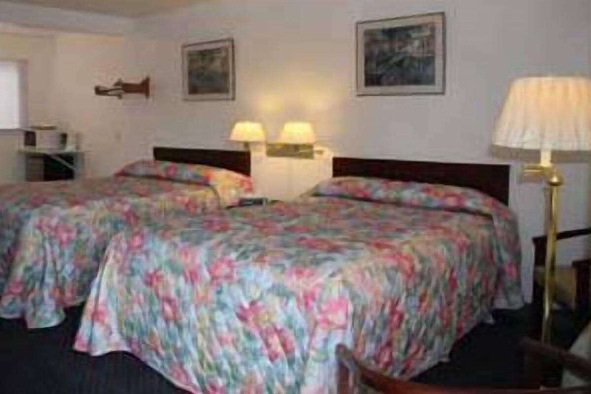 A hotel room with two beds, a desk, a chair, and two wall-mounted lamps.