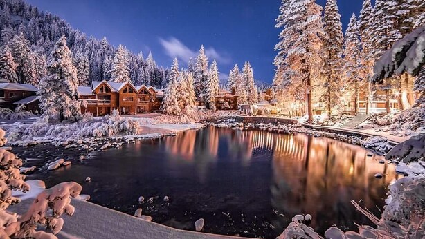 A winter scene with a wooden lodge, a pond, and snow-covered trees. - River Ranch Lodge & Restaurant (Olympic Valley)