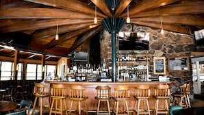 A rustic bar area with wooden beams, stone walls, and bar stools. - River Ranch Lodge & Restaurant (Olympic Valley)