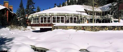 A snow-covered building with a stone wall and a glass enclosure.