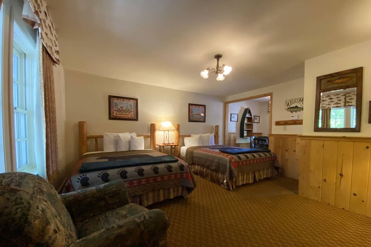 A hotel room with two beds, a wooden chair, a lamp, and a 'Welcome' sign.