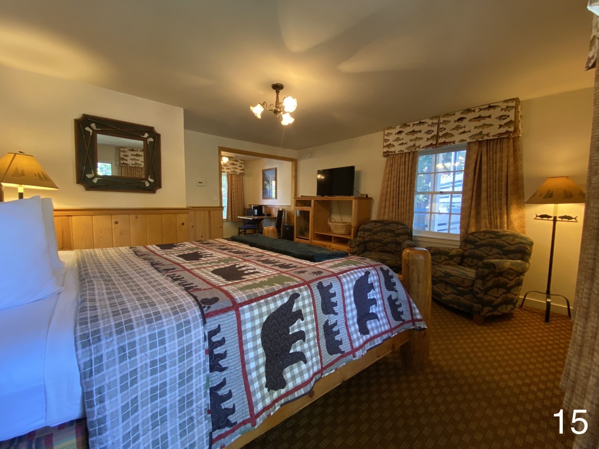 Una habitación de hotel con cama, una silla, un escritorio, televisor y ventana con cortinas.