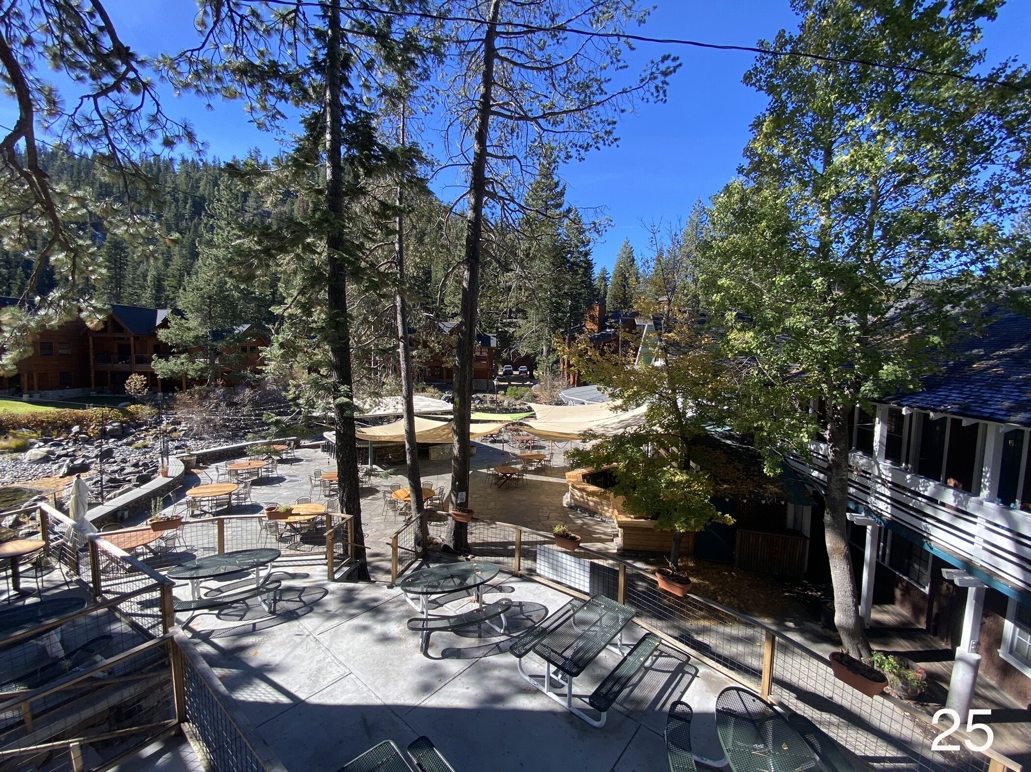 An outdoor patio area with tables and chairs, surrounded by trees and a building.