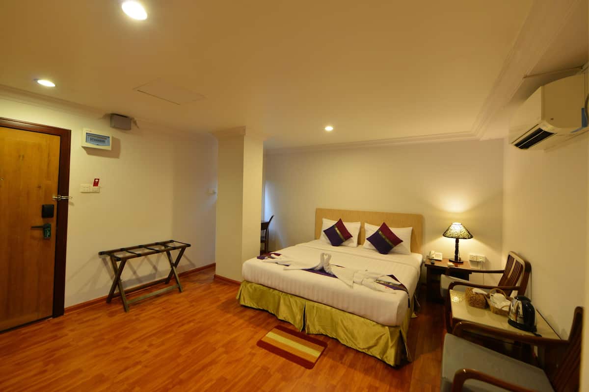 Habitación de hotel con cama, mesita de noche, silla y una pequeña mesa con lámpara.
