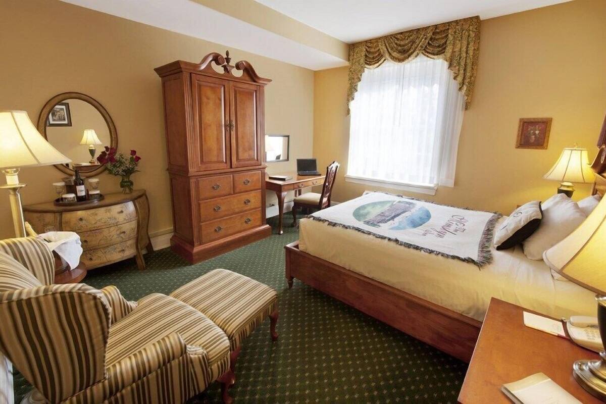 A hotel room with a bed, a desk, a chair, a wardrobe, and a window with curtains.