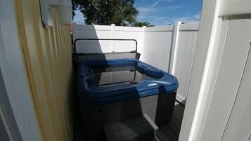 A hot tub with a black and blue exterior, positioned against a white fence, on a wooden deck.