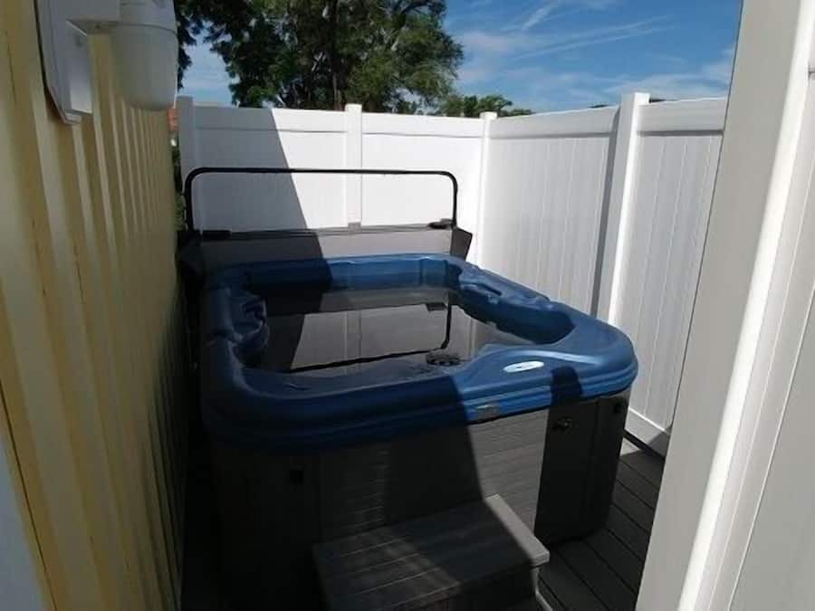 Ein Whirlpool mit schwarzer und blauer Außenverkleidung, vor einem weißen Zaun auf einer Holzterrasse.