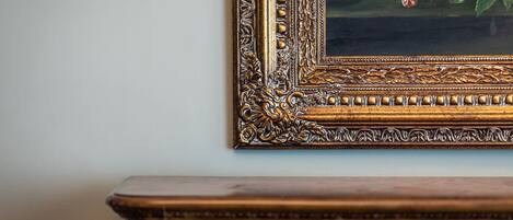 A framed painting with a floral design, mounted on a wall above a wooden dresser.
