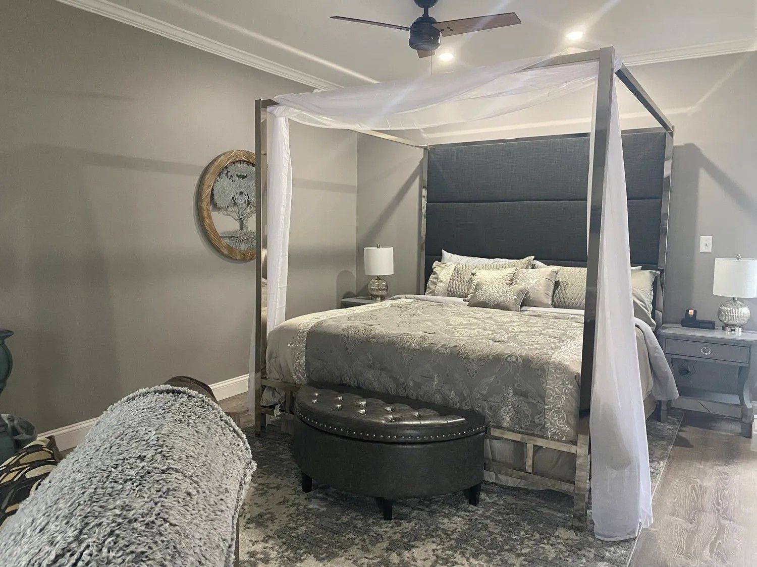 Un dormitorio con una cama con dosel, un espejo redondo, una mesita de noche con lámpara y una alfombra mullida.