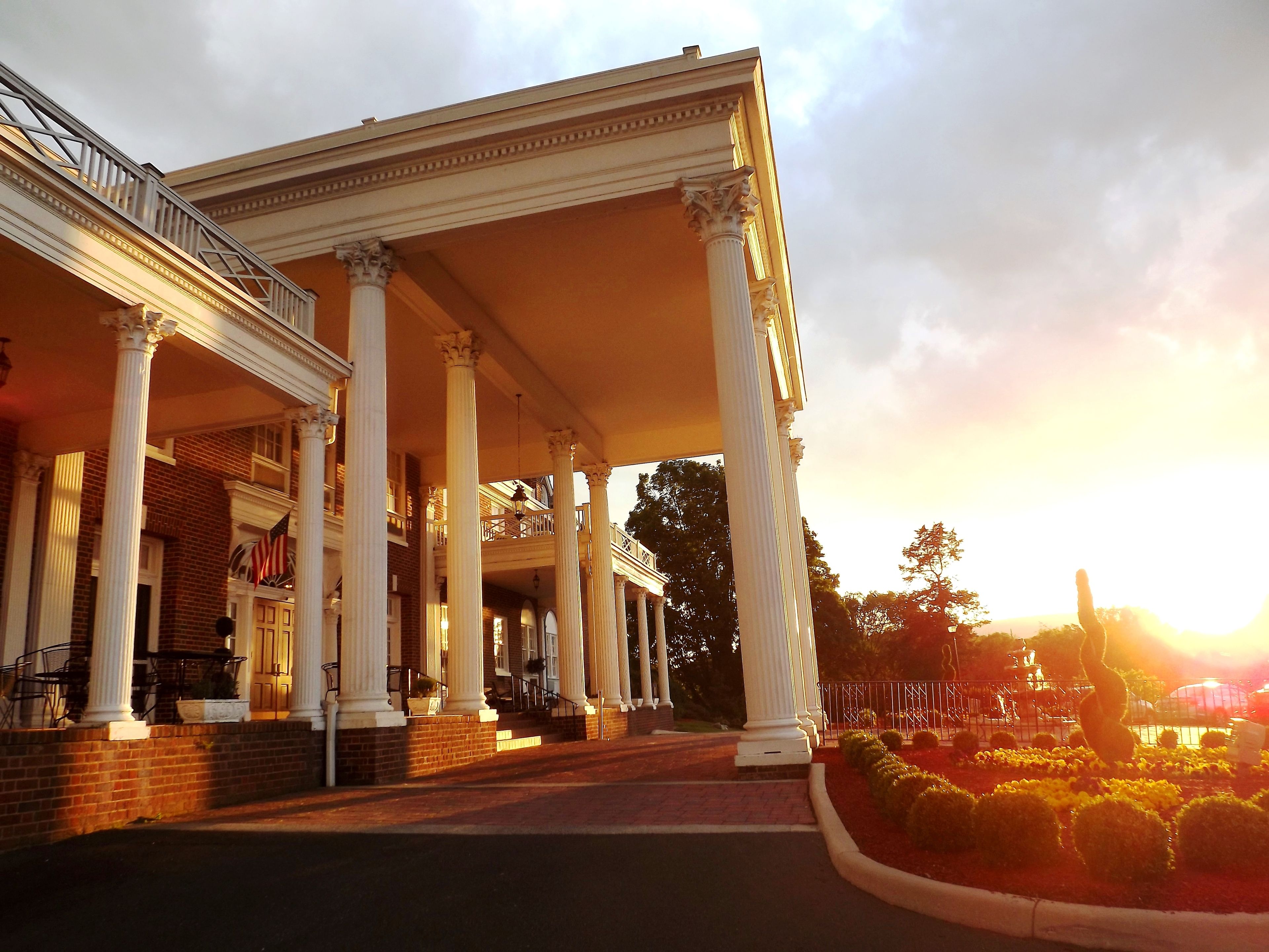 A building with a covered porch supported by columns, brick walls, and a flag.
