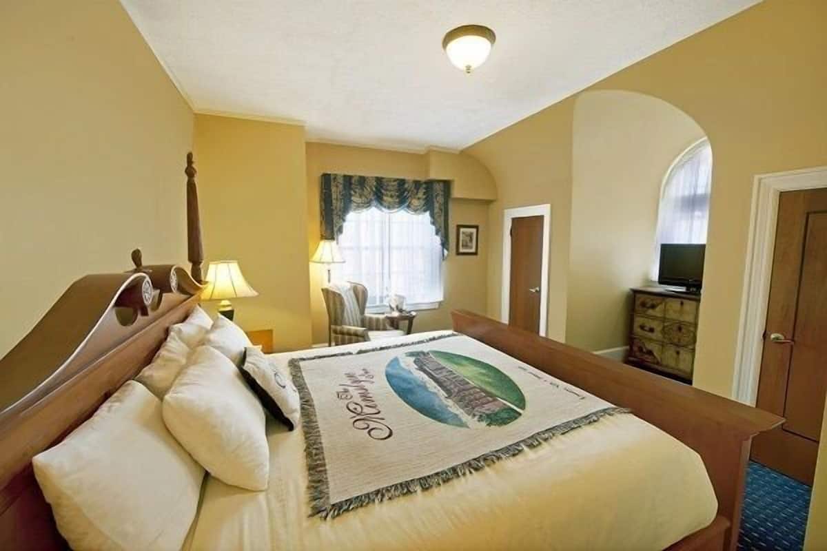 A hotel room with a bed, a lamp, a chair, a dresser, and a television.