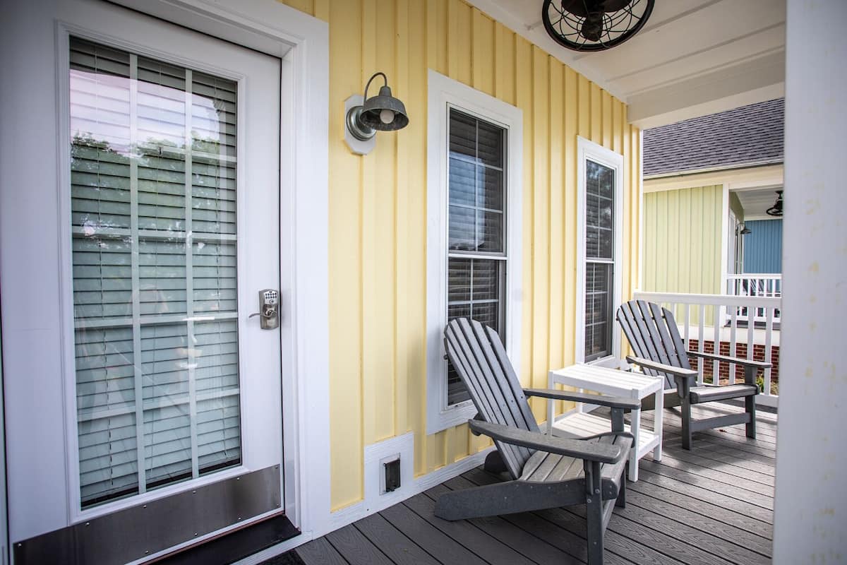 A yellow exterior with a covered porch, two Adirondack chairs, and a small table.