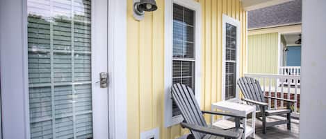 Fachada amarilla con un porche cubierto, dos sillas Adirondack y una mesita.