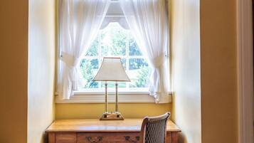 A room with a desk under a window with a lamp, a chair, and a sofa.