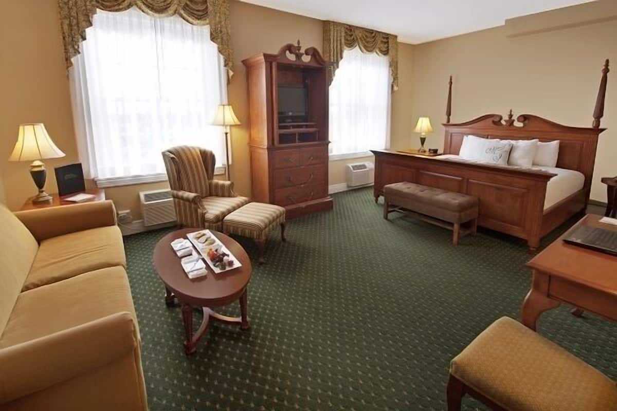 A hotel room with a bed, a sofa, a chair, a desk, and a television.