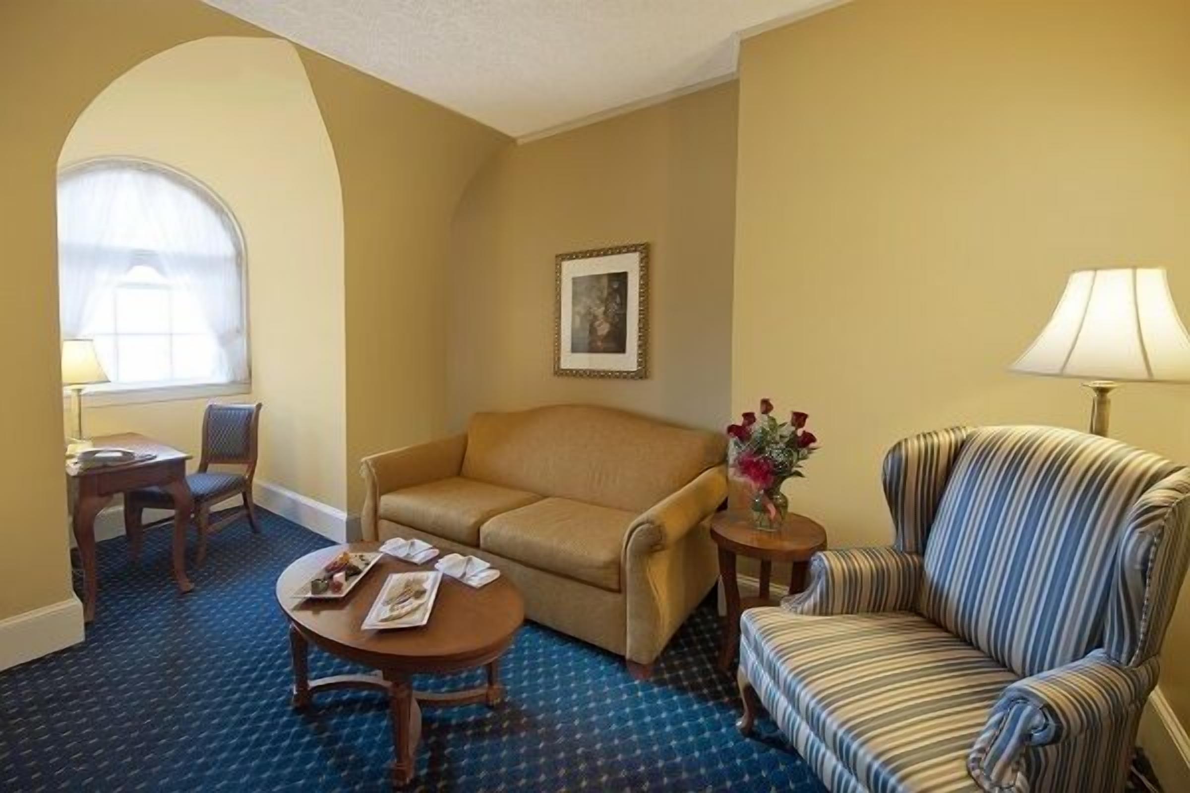 Habitación de hotel con sofá color beige, un sillón a rayas, una mesita con un florero y un cuadro en la pared.