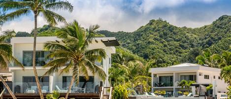 A modern resort with a pool, palm trees, and a mountainous backdrop.