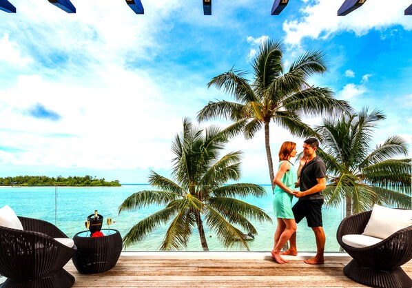 A couple standing by a poolside with a view of the ocean and palm trees.