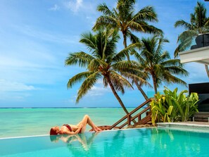 A woman relaxing by a pool with a view of the ocean and palm trees.