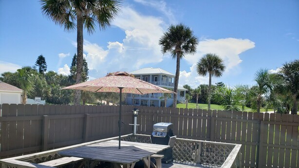 A wooden deck with a picnic table and grill, surrounded by a wooden fence and palm trees. - Studio 1 Motel (Daytona Beach)