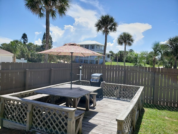 A wooden deck with a picnic table and grill, surrounded by a wooden fence and palm trees. - Studio 1 Motel (Daytona Beach)