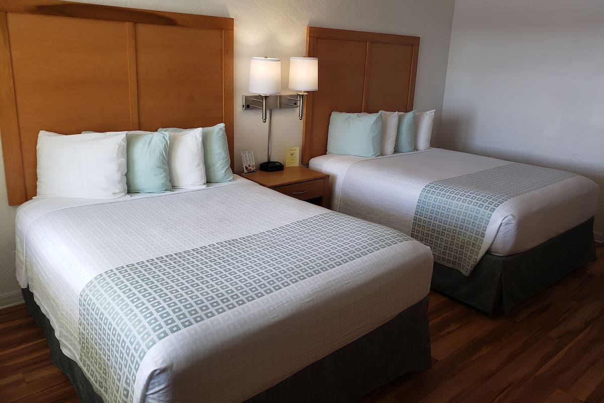 A hotel room with two beds, wooden headboards, bedside lamps, and a wooden floor.