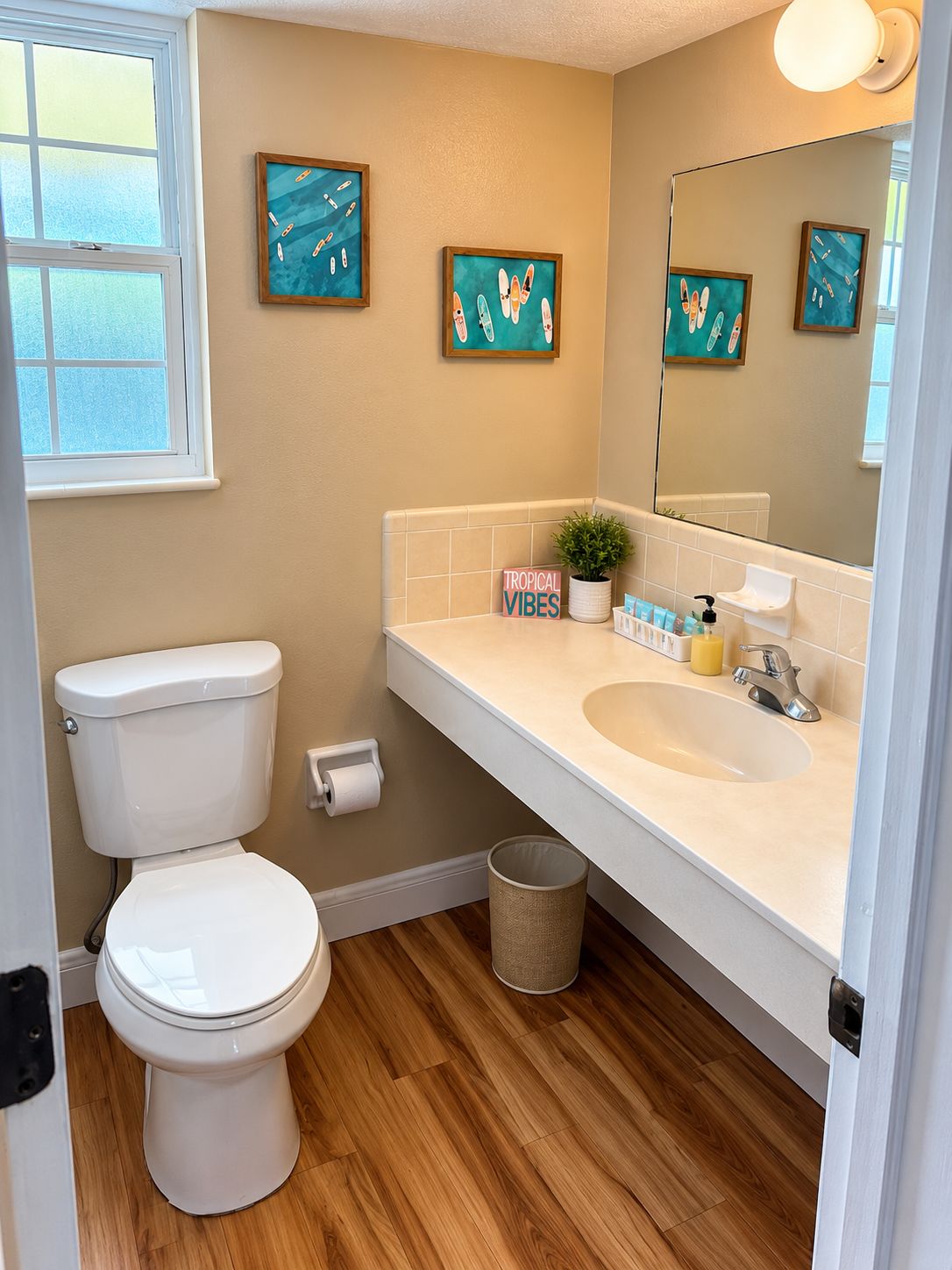 Une salle de bain avec des toilettes, un lavabo et un miroir. Des œuvres d’art encadrées ornent le mur, et une plante en pot est posée sur le comptoir.